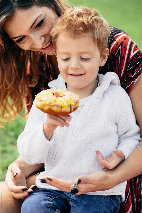 "Mother And Son At A Family Picnic, Eating A Doughnut" by Stocksy