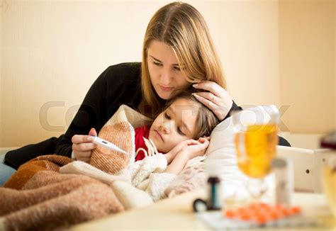 mother checking temperature of sick daughter lying in bed | Stock image ...