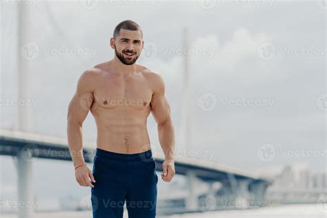 un hombre barbudo alegre y confiado con el torso desnudo mira con