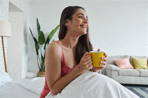 Happy young woman enjoying hot drink after waking up in bed 10153459