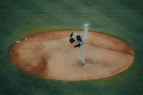 A baseball player pitching a ball on top of a field photo – Free Grey