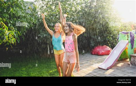 Photo of two happy laughing sisters in wet clothes dancing under water ...