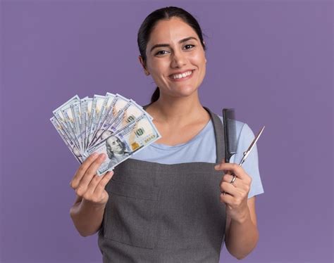 Fröhliche junge schöne Frau Friseur in der Schürze hält Bargeld und ...