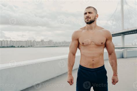 Young bearded athletic man with naked torso muscular body looks