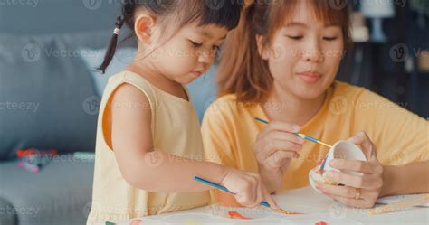 Happy cheerful Asia family mom teach toddler girl paint ceramic pot