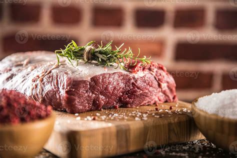 Raw beef ribe-eye steak with salt pepper and herbs on wooden butcher