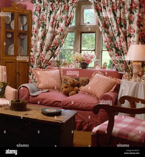 Floral curtains on window behind a pink sofa in country living room with an old pine chest used ...