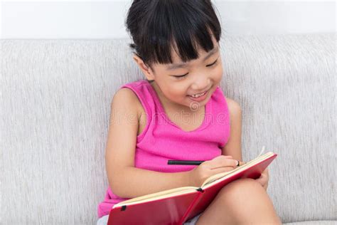 Счастливая азиатская китайская маленькая девочка сидя на книге ...