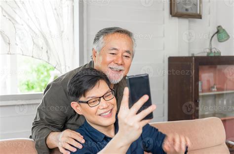 Happy senior asian father and adult son using smart phone talking on