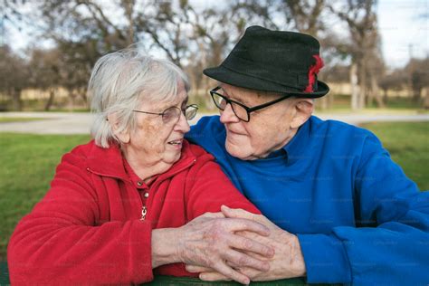 An older couple sitting on a bench in a park photo – Holding hands
