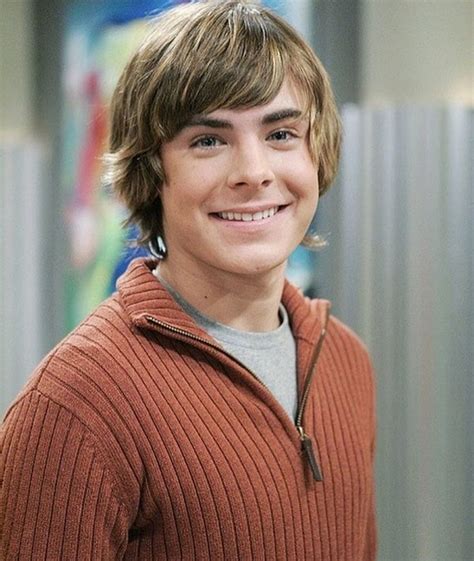 a young man in an orange sweater smiles at the camera