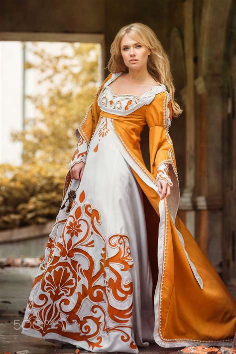 Beautiful blond woman in medieval dress walking near old building ...