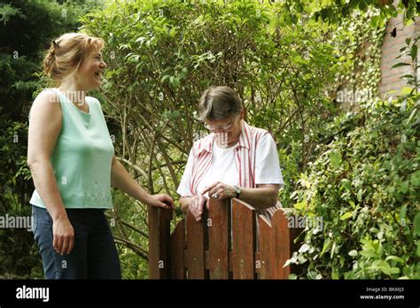 Two adult women, neigbours, talking over fence. The neighbors have a 