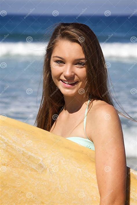 Beautiful Teenage Girl Holding a Surfboard at the Beach Smiling Stock