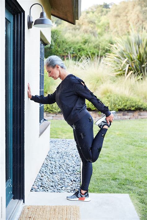 "Mature Woman With Grey Hair Stretching In Backyard For Fitness Run" by