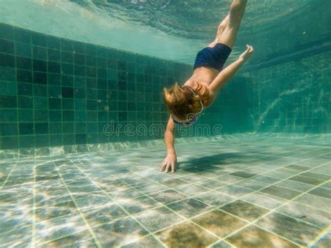 Мальчик ребенка плавает под водой в бассейне, усмехается и держится ...