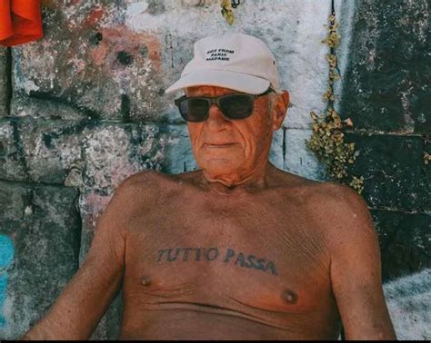 an old man with tattoos on his chest sitting in front of a brick wall