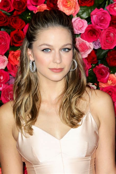 a woman with long hair and blue eyes standing in front of flowers