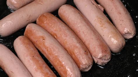 Close up of meat sausages fried in black pan with oil. View of cooking
