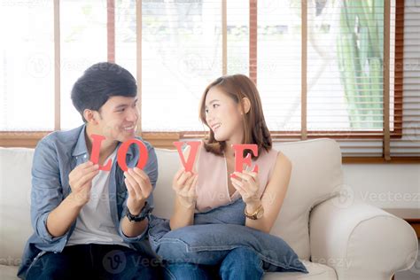 Beautiful young asian couple sitting on sofa holding word love together