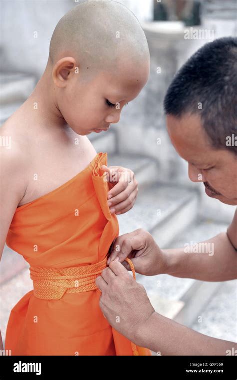 Old Buddhist monk helps young novice monk wearing yellow robe during ...