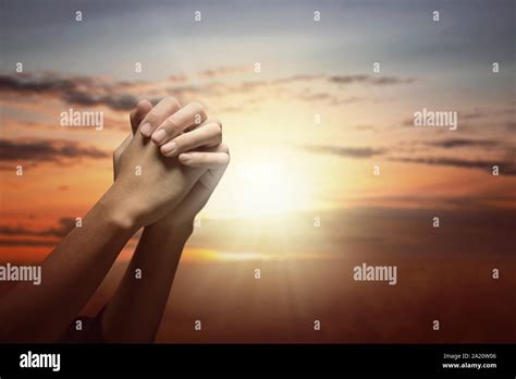 Human hands raised while praying to god with a sunset sky background ...