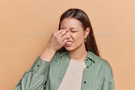 Tired brunette woman touching nose between closed eyes suffers from eye tension after working on ...