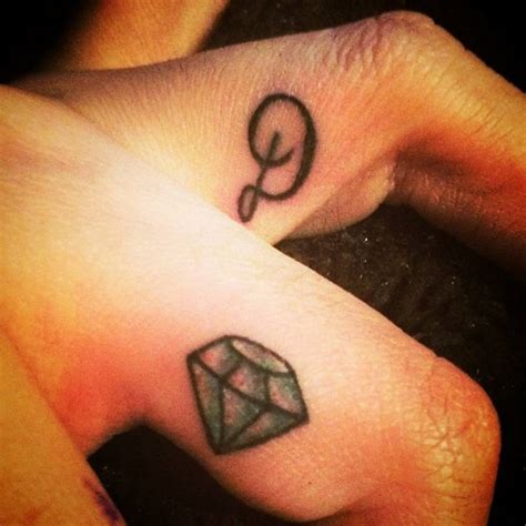 Finger tattoos of a diamond and the initial “D”.