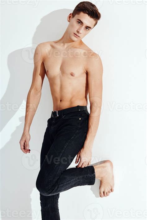 Handsome guy with a naked torso stands on one leg against the wall