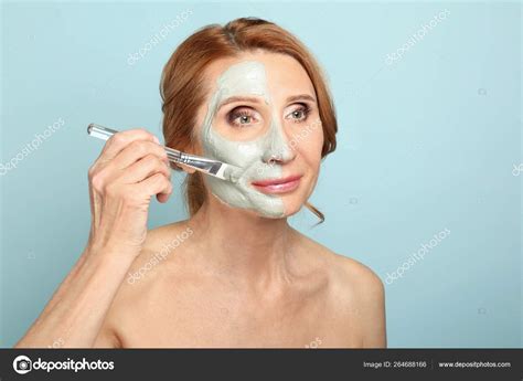 Mature woman applying facial mask against color background Stock Photo