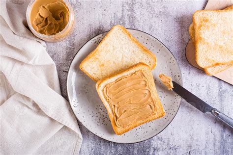 Peanut butter sandwich on toasted bread on a plate and jar of butter on the table. Top view ...