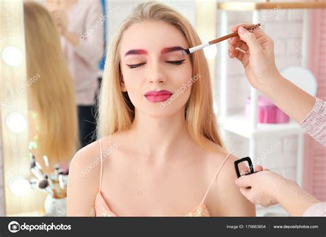 Professional artist creating makeup for beautiful model in room Stock ...