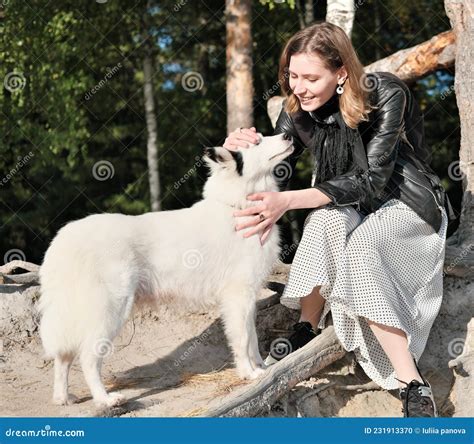 Front View of Young Smiling Woman Stroking Her Dog Whle Sitting Under