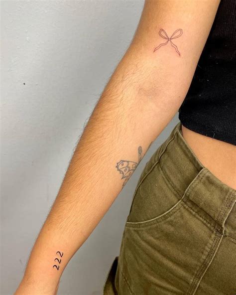 Number "222" and ribbon tattoos located on the wrist