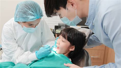 Asian female pediatric dentist checks and examines girl's teeth with