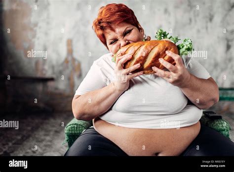 Fette Frau sitzt in einem Sessel und isst Sandwich, bulimic und ...