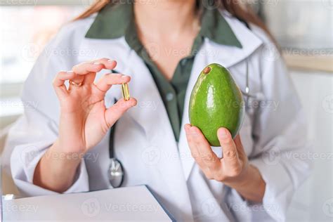Nutritionist in white coat holding avocado and capsule of dietary