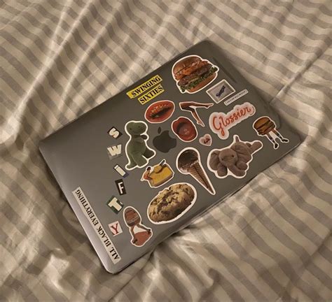 an open laptop computer sitting on top of a bed covered in lots of stickers